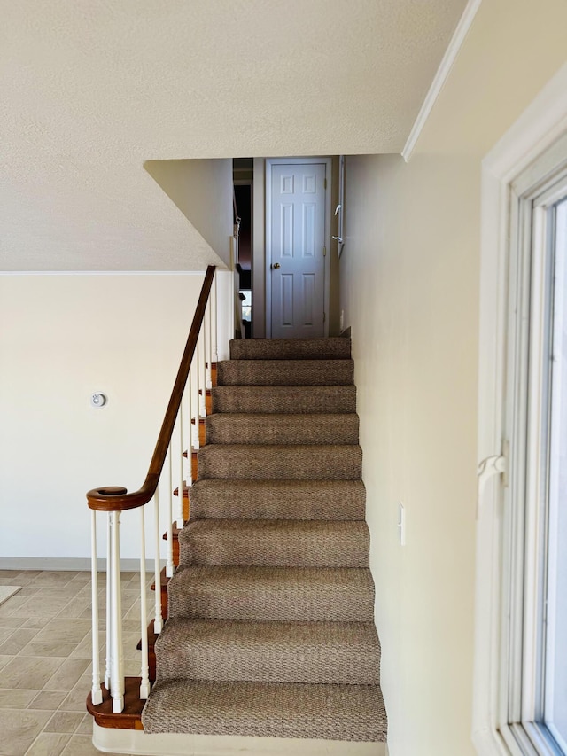 staircase with baseboards, ornamental molding, and a textured ceiling