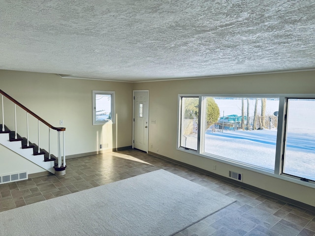 foyer featuring visible vents, a textured ceiling, baseboards, and stairs