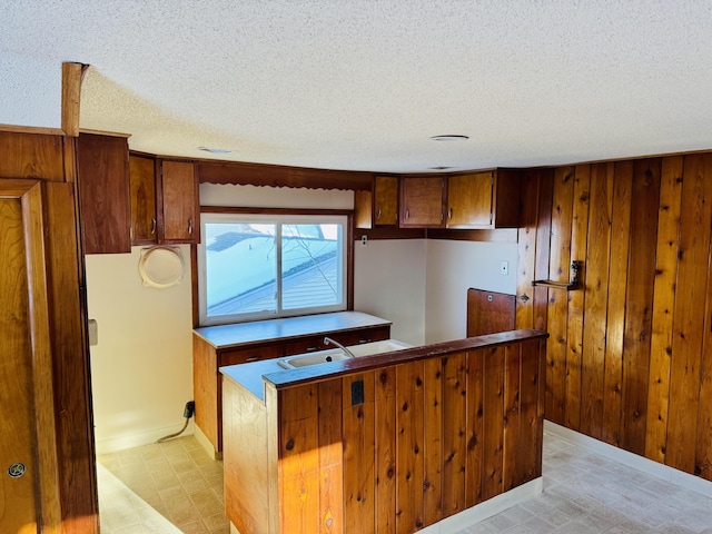 kitchen with a textured ceiling, light floors, wood walls, and brown cabinetry