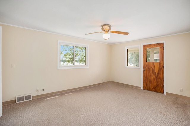 carpeted empty room with baseboards, visible vents, a ceiling fan, and ornamental molding