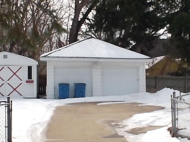 snow covered garage with a detached garage and fence