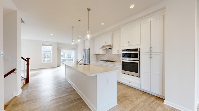 kitchen with stainless steel appliances, white cabinets, hanging light fixtures, and an island with sink