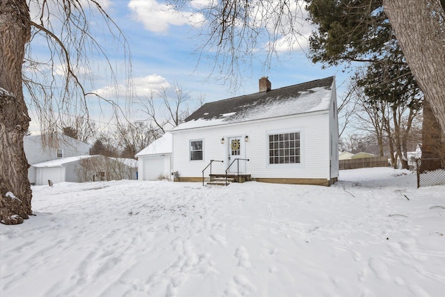 snow covered back of property featuring a garage, fence, and a chimney