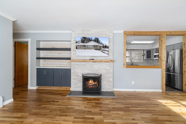 unfurnished living room featuring wood finished floors, a fireplace, a sink, and crown molding