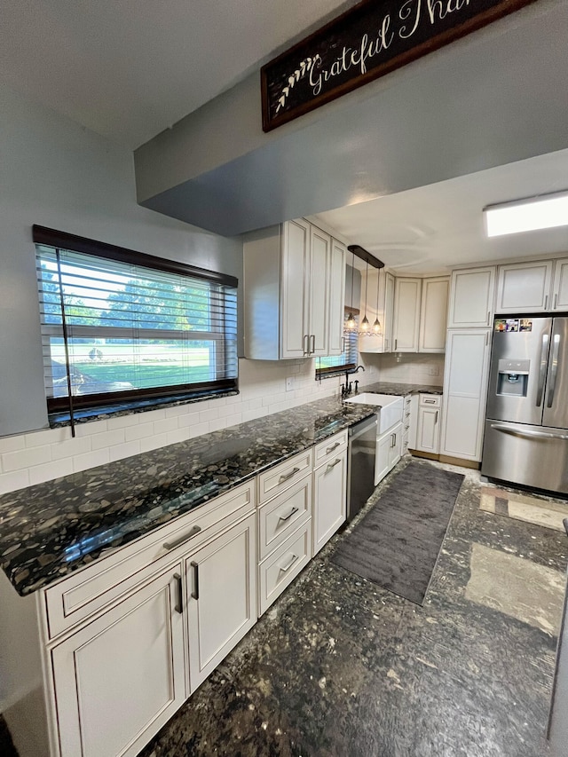 kitchen featuring decorative backsplash, white cabinets, appliances with stainless steel finishes, dark stone countertops, and hanging light fixtures