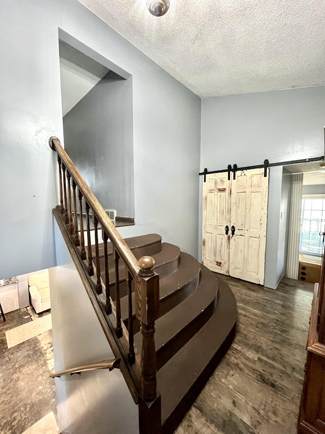 stairs featuring a textured ceiling, a barn door, and wood finished floors