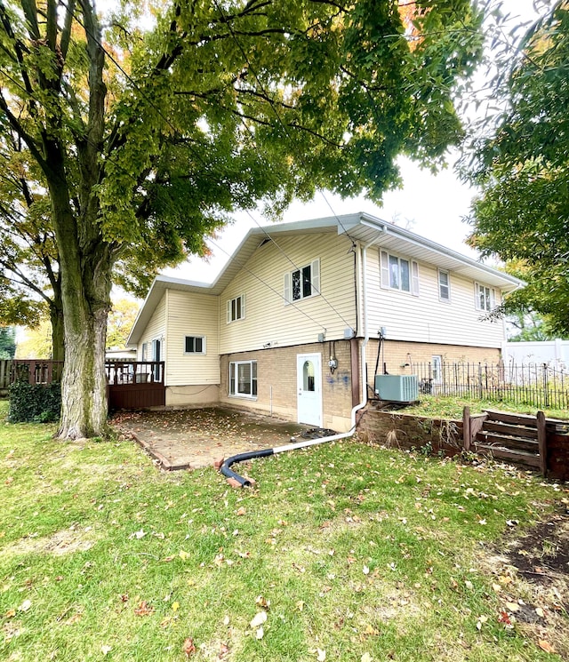 rear view of house with brick siding, a lawn, cooling unit, and fence