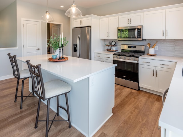 kitchen featuring a kitchen bar, stainless steel appliances, light wood-style floors, white cabinets, and light countertops