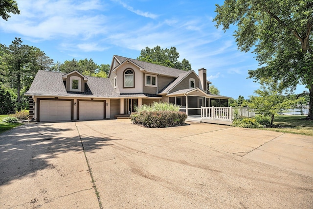 view of front of house with driveway, a garage, a sunroom, a chimney, and roof with shingles