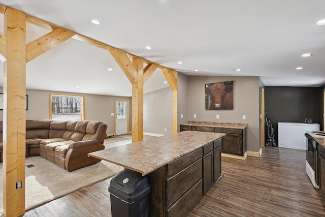 kitchen with a kitchen island, open floor plan, dark wood-style flooring, vaulted ceiling, and light countertops