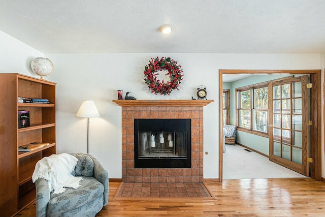 living area with visible vents, baseboards, light wood finished floors, and a tiled fireplace