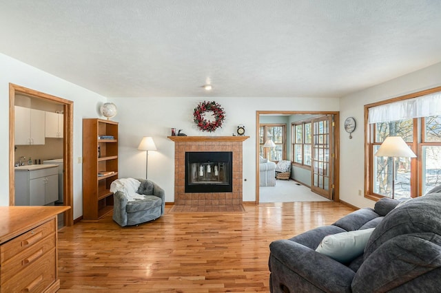 living area with a textured ceiling, light wood finished floors, a fireplace, and baseboards