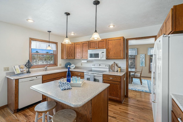 kitchen featuring white appliances, brown cabinets, decorative light fixtures, light countertops, and a sink