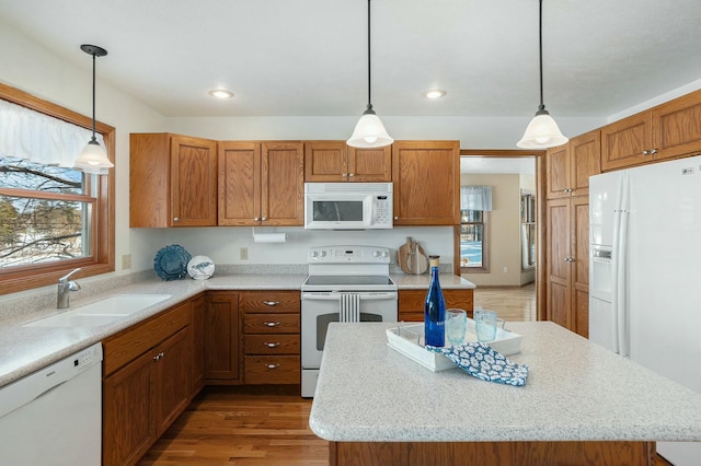 kitchen featuring hanging light fixtures, white appliances, brown cabinetry, and a sink