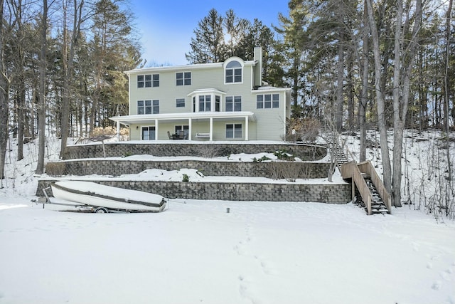 snow covered back of property featuring stairs, a chimney, and a porch