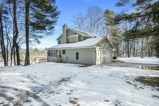 view of snowy exterior with a garage and a chimney