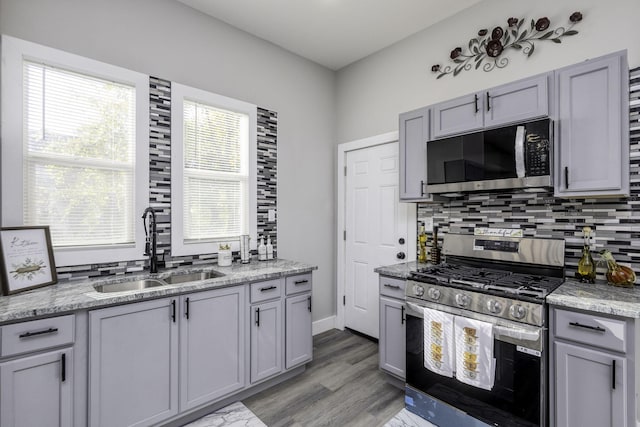 kitchen featuring light stone counters, decorative backsplash, stainless steel appliances, and a sink