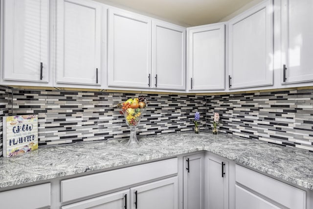 kitchen featuring light stone counters, tasteful backsplash, and white cabinetry