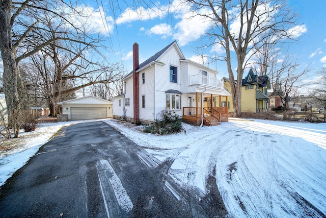 view of snowy exterior featuring a garage, an outbuilding, and a chimney