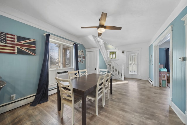 dining room with a baseboard heating unit, ceiling fan, stairway, and wood finished floors