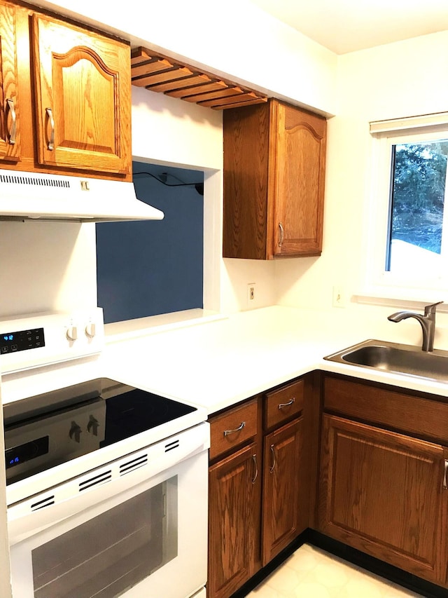 kitchen featuring electric stove, light countertops, brown cabinetry, a sink, and under cabinet range hood