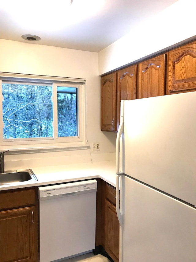 kitchen with brown cabinets, white appliances, light countertops, and a sink