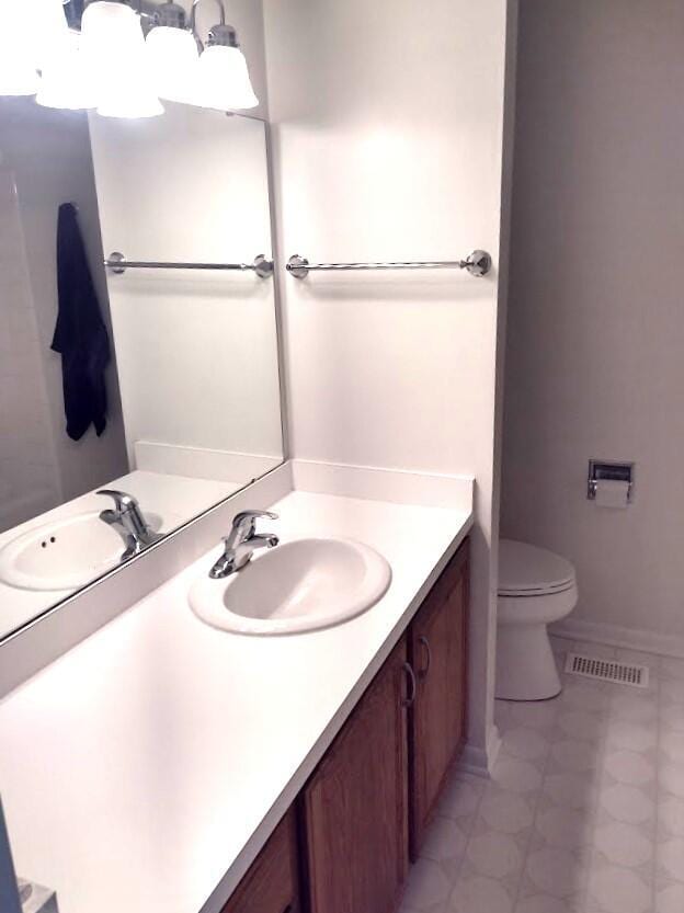 bathroom with toilet, vanity, visible vents, and baseboards