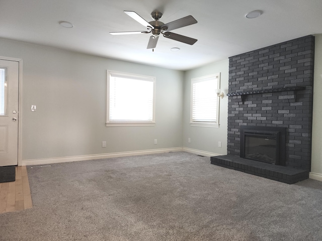 unfurnished living room with carpet floors, a brick fireplace, baseboards, and a ceiling fan