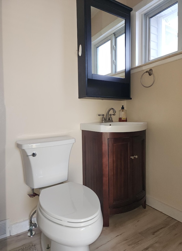 half bath with baseboards, visible vents, toilet, wood finished floors, and vanity