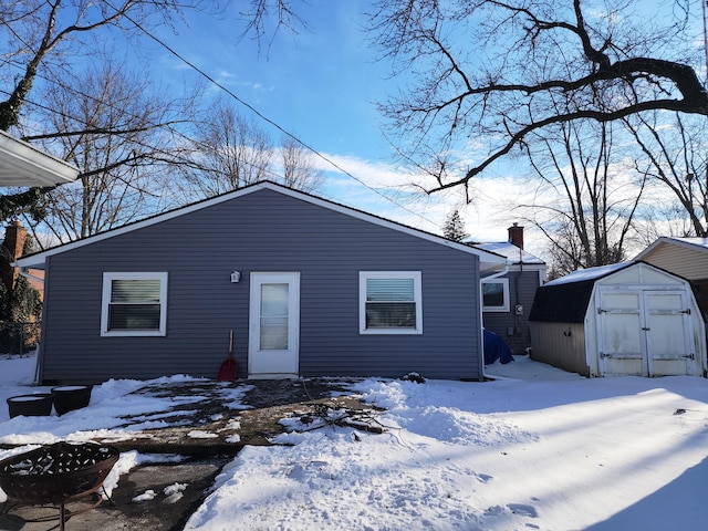 snow covered house with an outdoor structure, a chimney, and a shed