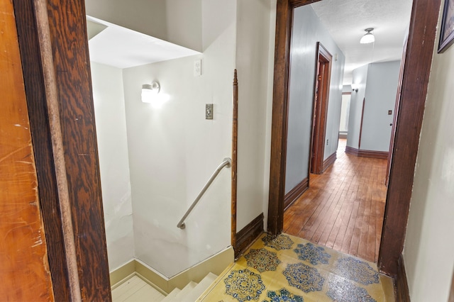 hallway with baseboards, a textured ceiling, an upstairs landing, and wood finished floors