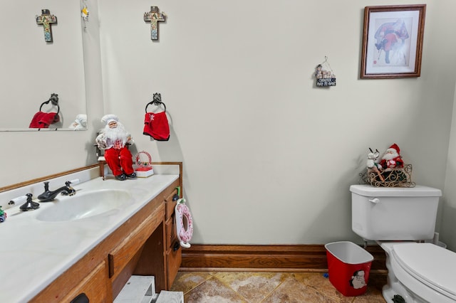 half bath with toilet, baseboards, and vanity