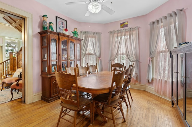 dining space with light wood-type flooring, ceiling fan, stairway, and baseboards