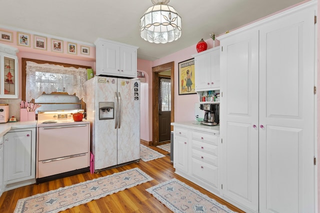 kitchen featuring light wood finished floors, light countertops, white appliances, and white cabinetry