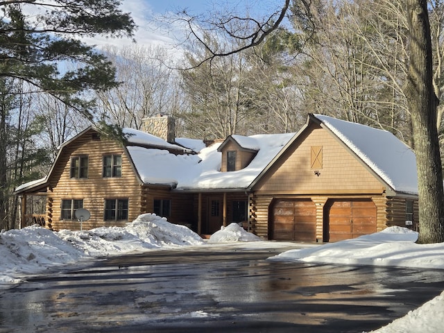 cabin featuring driveway, a chimney, an attached garage, and log siding