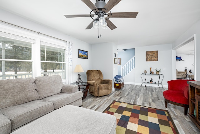 living room with ceiling fan, stairway, baseboards, and wood finished floors