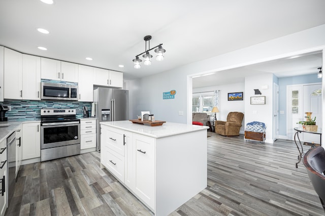 kitchen featuring stainless steel appliances, backsplash, open floor plan, white cabinets, and wood finished floors