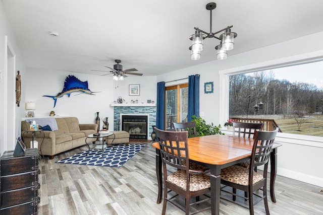 dining area featuring light wood finished floors, a fireplace, baseboards, and ceiling fan with notable chandelier