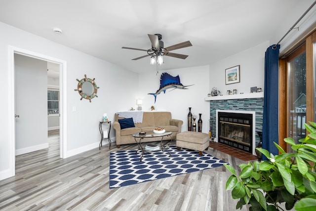 living room featuring ceiling fan, a fireplace, baseboards, and wood finished floors