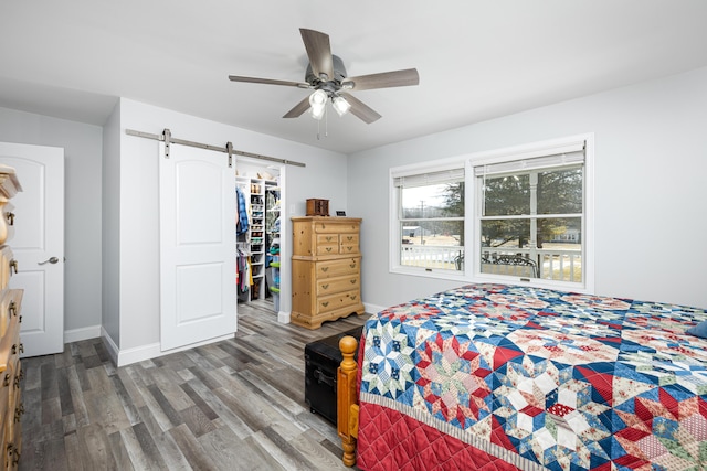 bedroom with a closet, a spacious closet, a barn door, wood finished floors, and baseboards