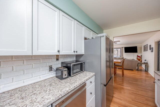 kitchen with white cabinets, appliances with stainless steel finishes, open floor plan, light stone countertops, and light wood-style floors