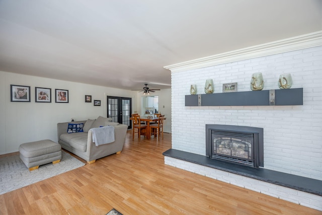 living area featuring a brick fireplace, ceiling fan, wood finished floors, and french doors