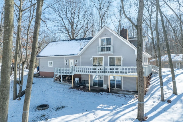 snow covered back of property with a deck and a chimney