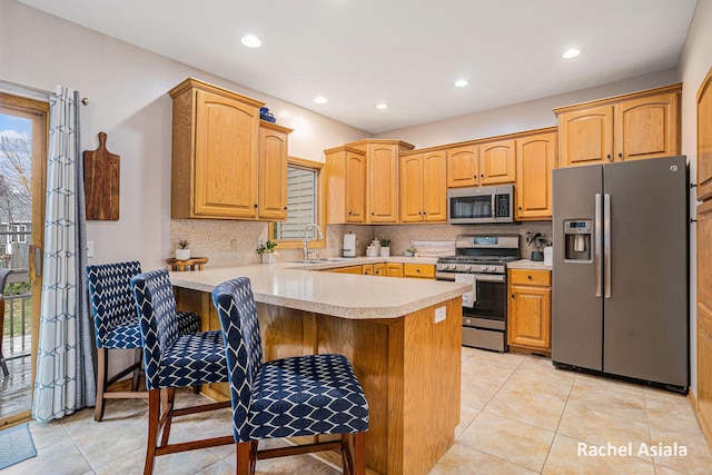 kitchen featuring decorative backsplash, a peninsula, stainless steel appliances, light countertops, and a sink