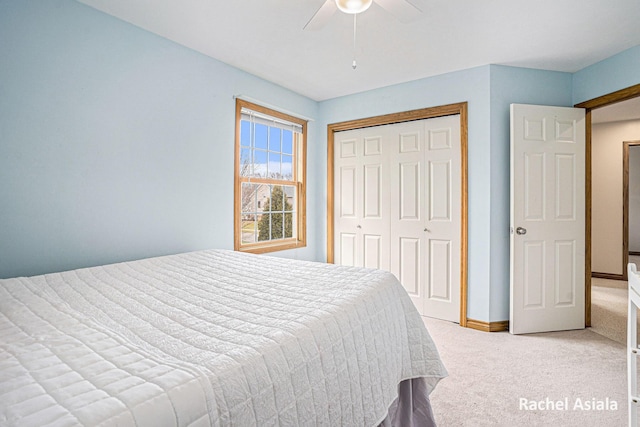 bedroom with a ceiling fan, a closet, light colored carpet, and baseboards