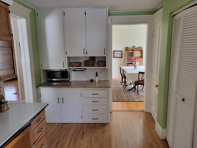 kitchen with light stone counters, white cabinetry, stainless steel microwave, and light wood finished floors