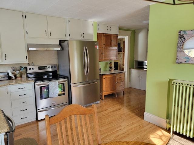 kitchen with light stone counters, stainless steel appliances, white cabinetry, range hood, and radiator