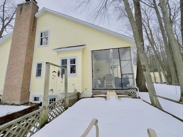 snow covered house featuring a sunroom and a chimney