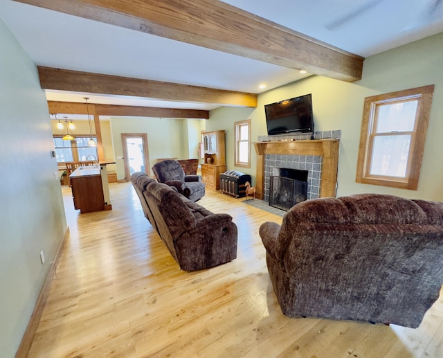 living room featuring baseboards, a fireplace, beam ceiling, and light wood-style floors