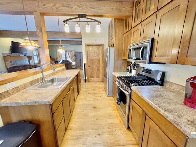 kitchen featuring a sink, light wood-style floors, light countertops, appliances with stainless steel finishes, and hanging light fixtures